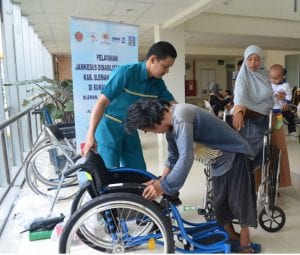 Salah seorang disabilitas menerima kursi roda baru bersama Eko Kurniawan, A.Md.O, Staf RS UGM